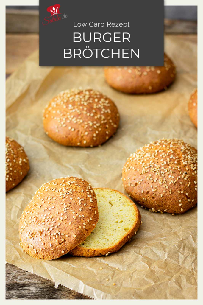  Burgerbr&ouml;tchen mit Sesamtopping auf Backpapier, ein halbiertes Br&ouml;tchen zeigt die Innenstruktur
