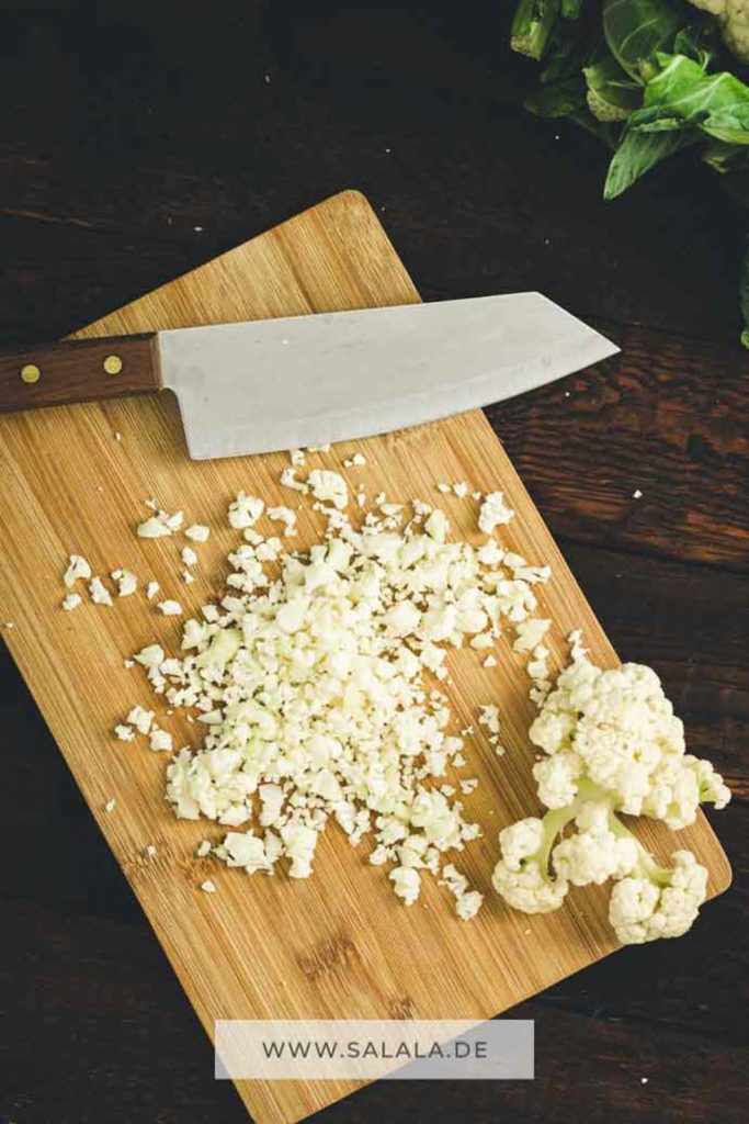 Holzbrett mit gehacktem Blumenkohlreis und scharfem Messer