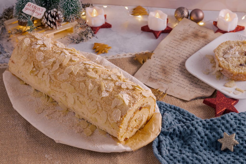 Eine Low Carb Bratapfelbiskuitrolle, umrahmt von Weihnachtsdekoration und Kerzen