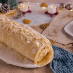 Eine Low Carb Bratapfelbiskuitrolle, umrahmt von Weihnachtsdekoration und Kerzen