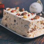 Kastenförmiges Stollen Parfait mit cremiger Textur und sichtbaren Nüssen und Früchten, serviert auf länglichem weißem Teller