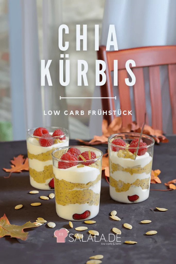 Chia Kürbis Dessert Pin 3 Low Carb Rezept drei Gläser mit dem Chia-Kürbis Dessert auf einem schwarzen Holztisch, umgeben von bunten Herbstblättern und Kürbiskernen. Im Hintergrund ist ein Fenster mit weißen Vorhängen und ein Holzstuhlauf dem Bild selbst steht der Text: "Chia Kürbis Low Carb Frühstück salala.de"