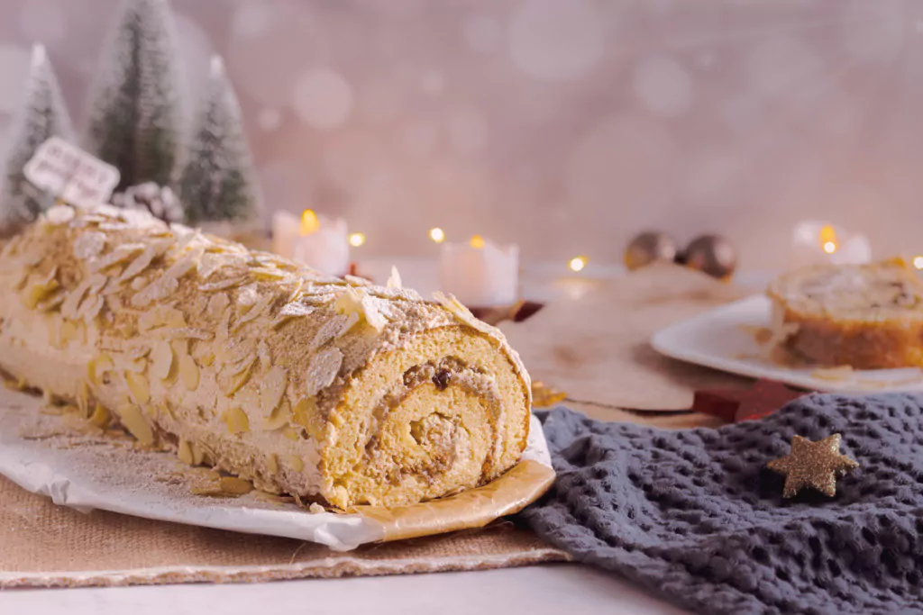 Eine Low Carb Bratapfelbiskuitrolle, umrahmt von Weihnachtsdekoration und Kerzen