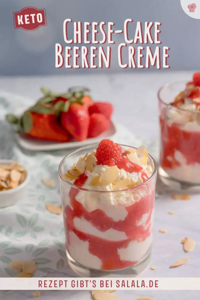 Zwei Gl&auml;ser mit cremiger Cheesecake-Creme und Beerensauce, dekoriert mit Himbeeren und Mandeln auf einer gemusterten Tischdecke.