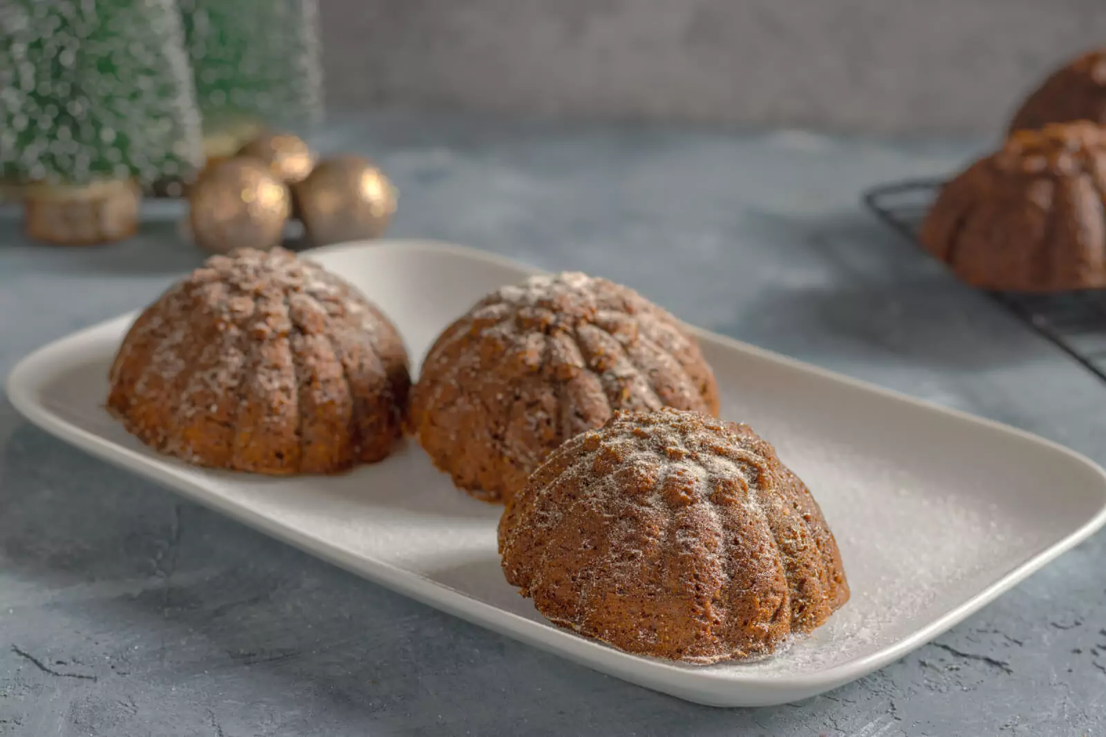 rei weihnachtliche Low Carb Lebkuchen-K&uuml;chlein auf einem wei&szlig;en Teller, leicht mit Puderzucker best&auml;ubt. Im Hintergrund sind verschwommene Weihnachtskugeln und Tannendeko zu erkennen.